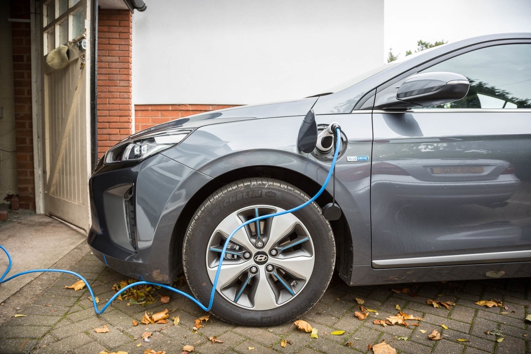 Grå hybridbil som laddas på en uppfart bredvid ett garage.